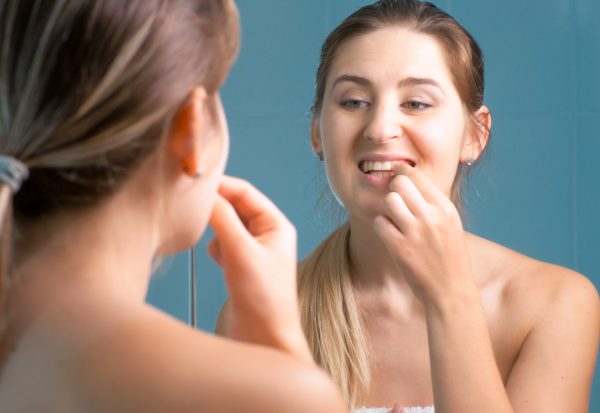 Young woman cleaning and checking her teeth at mirror in bathroom.